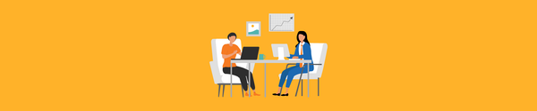 Two women sitting across a desk working on laptops with charts on the wall behind them.